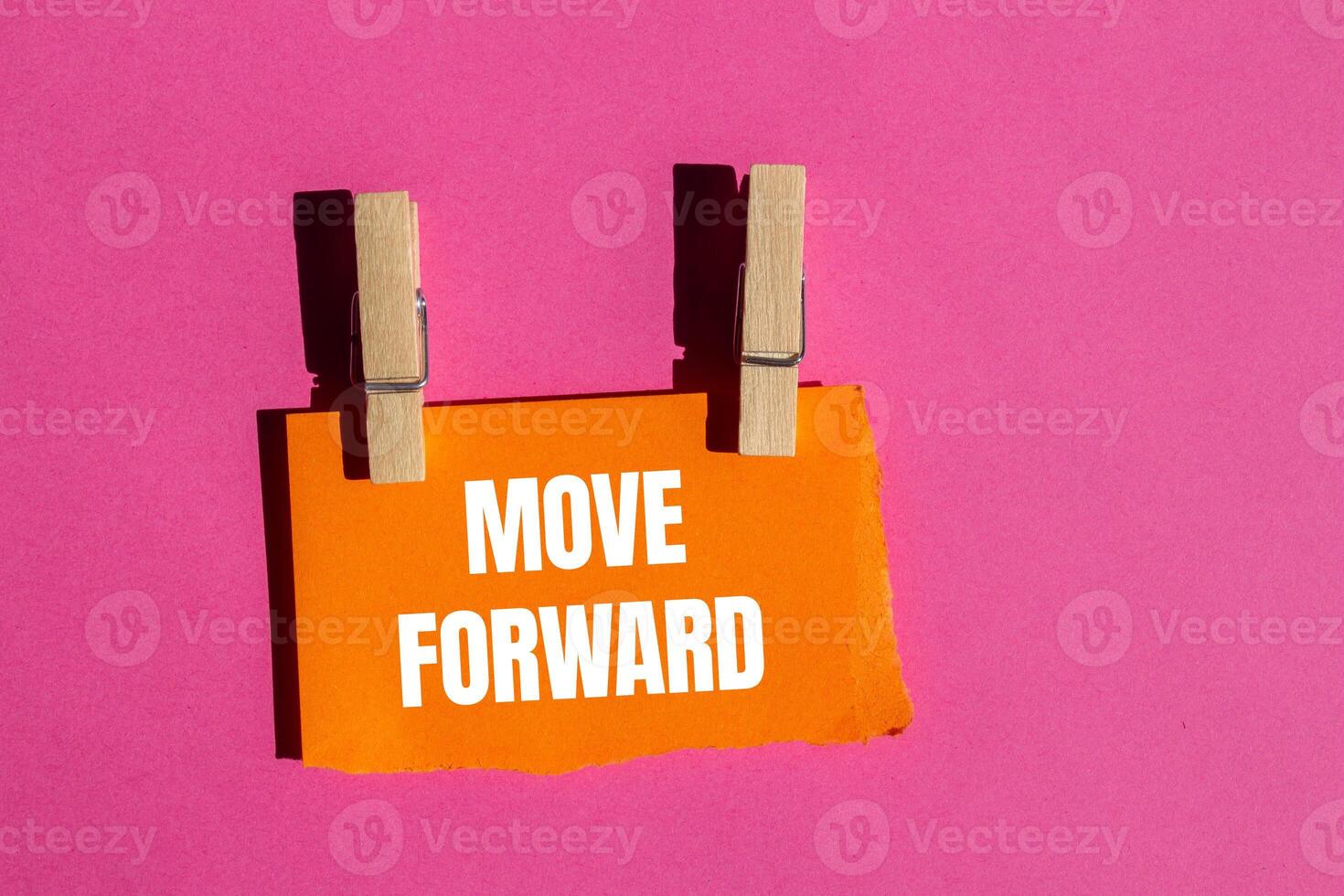 Move forward message written on ripped torn orange paper piece with pink background. Conceptual move forward symbol. Copy space. photo