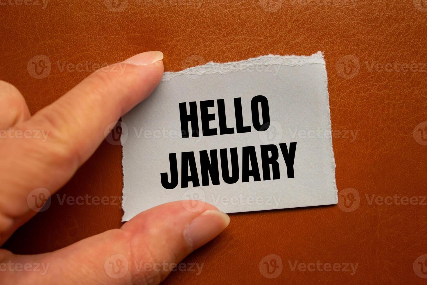 Hello january message written on ripped torn paper piece with brown background. Conceptual hello january symbol. Copy space. photo