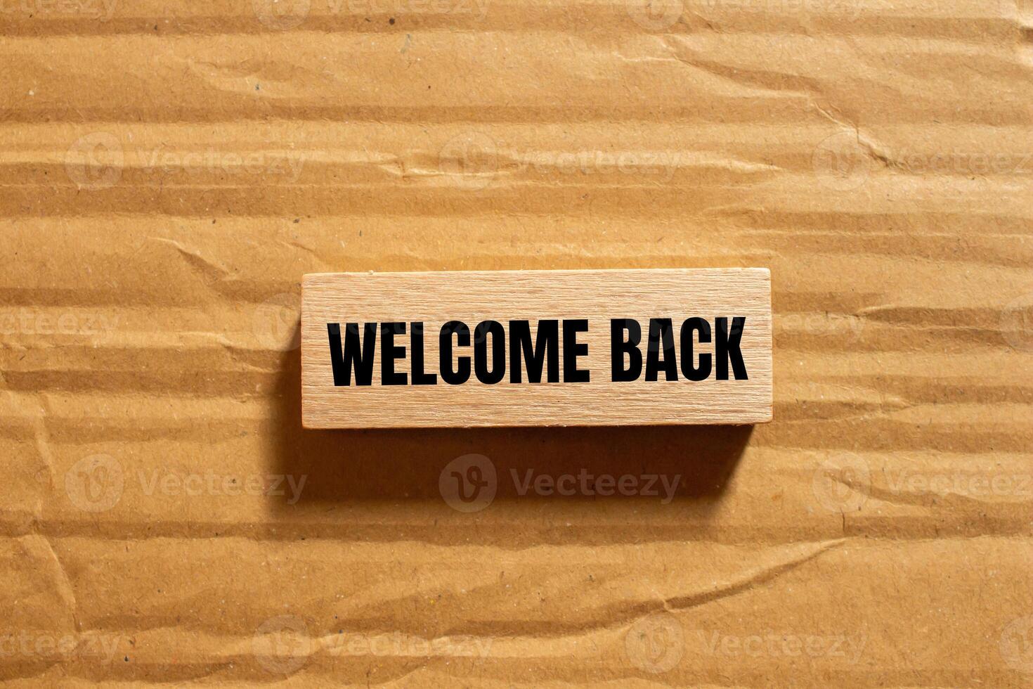 Welcome back message written on wooden block with cardboard background. Conceptual welcome back symbol. Copy space. photo