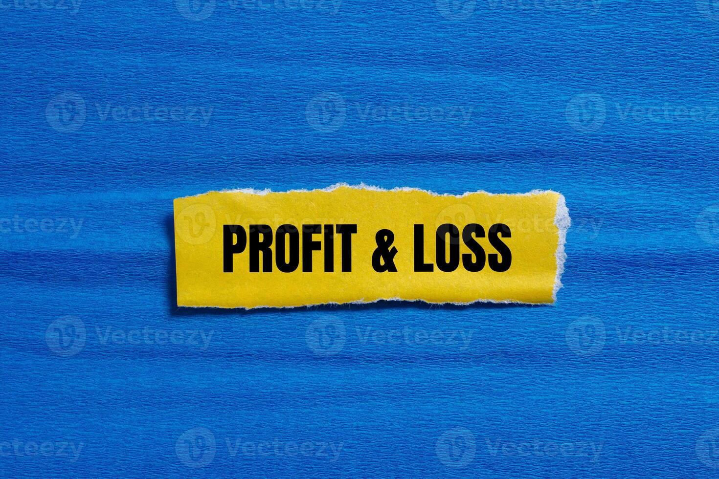 Profit and loss message written on ripped torn yellow paper piece with blue background. Conceptual profit and loss symbol. Copy space. photo