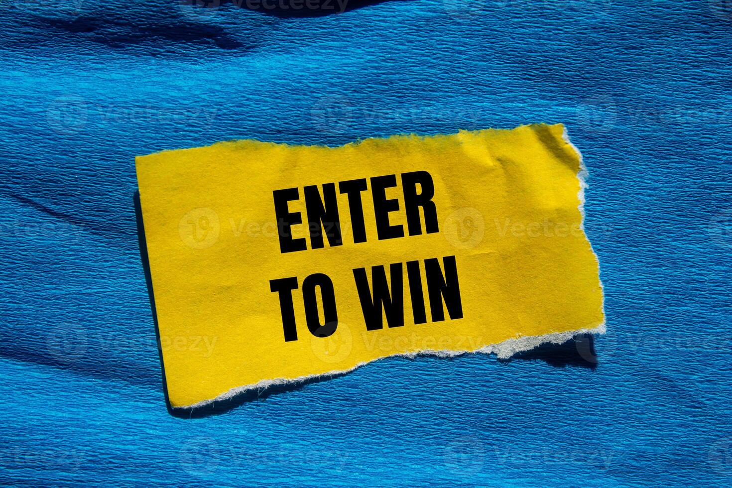 Enter to win message written on ripped torn yellow paper piece with blue background. Conceptual enter to win symbol. Copy space. photo
