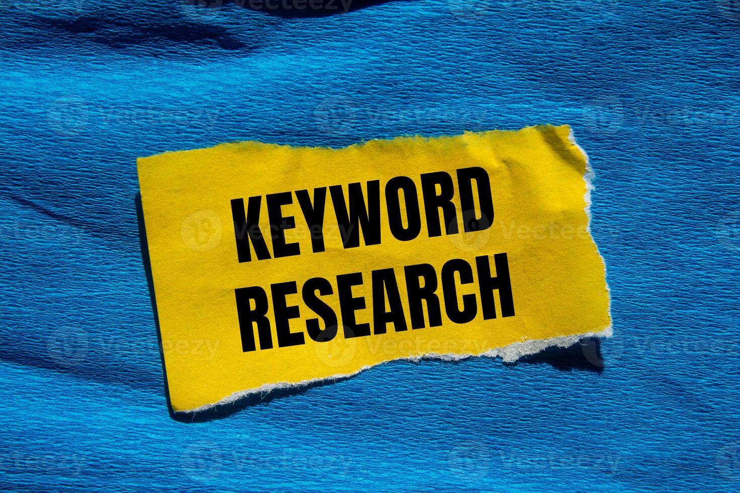 Keyword research message written on ripped torn yellow paper piece with blue background. Conceptual keyword research symbol. Copy space. photo