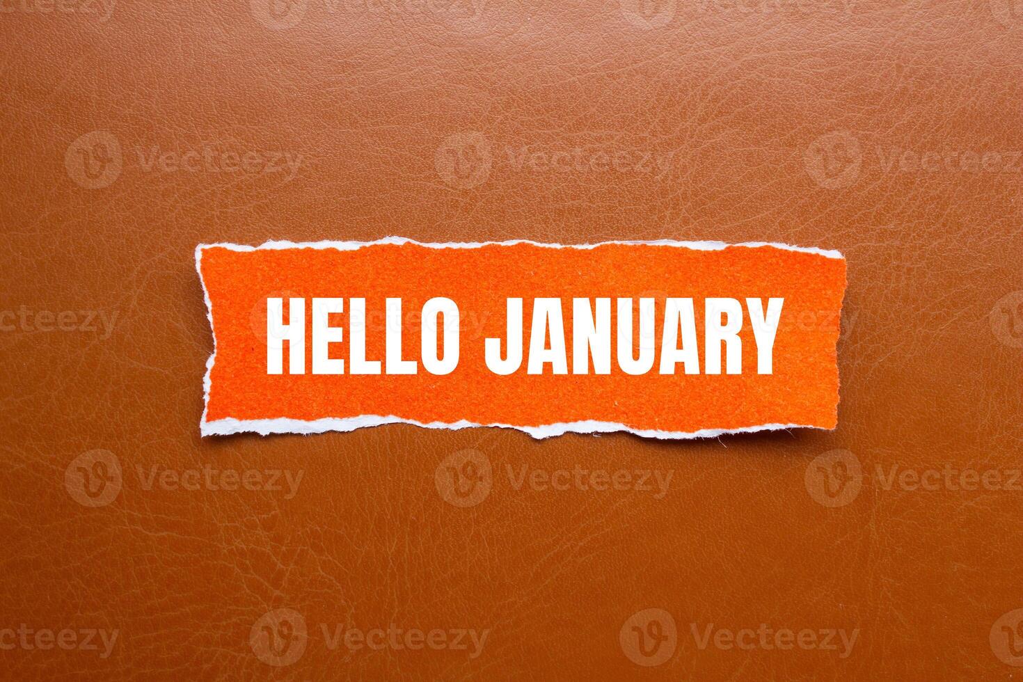 Hello january message written on ripped orange torn paper piece with brown background. Conceptual hello january symbol. Copy space. photo