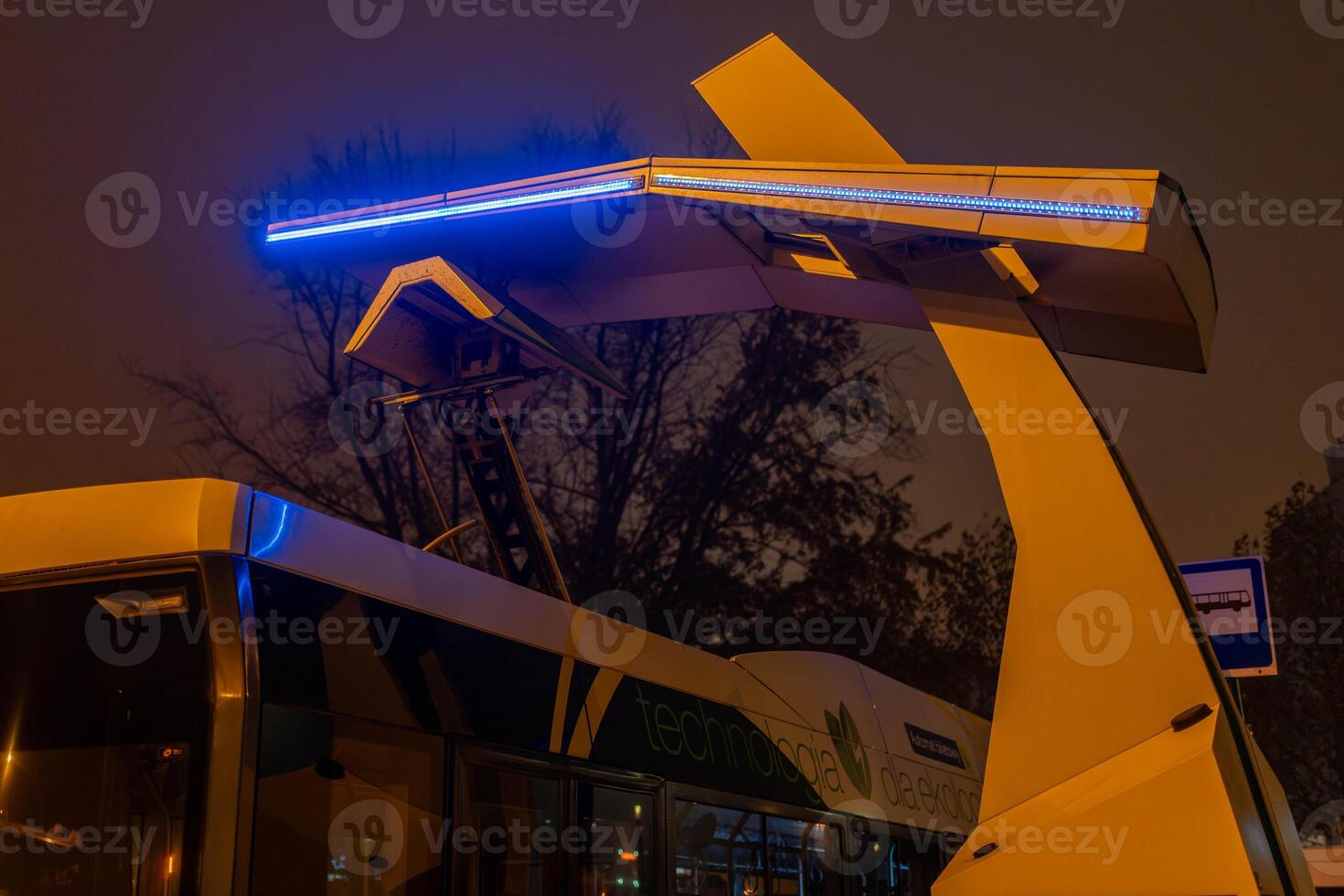 An electric bus is charged at a charging station at night photo