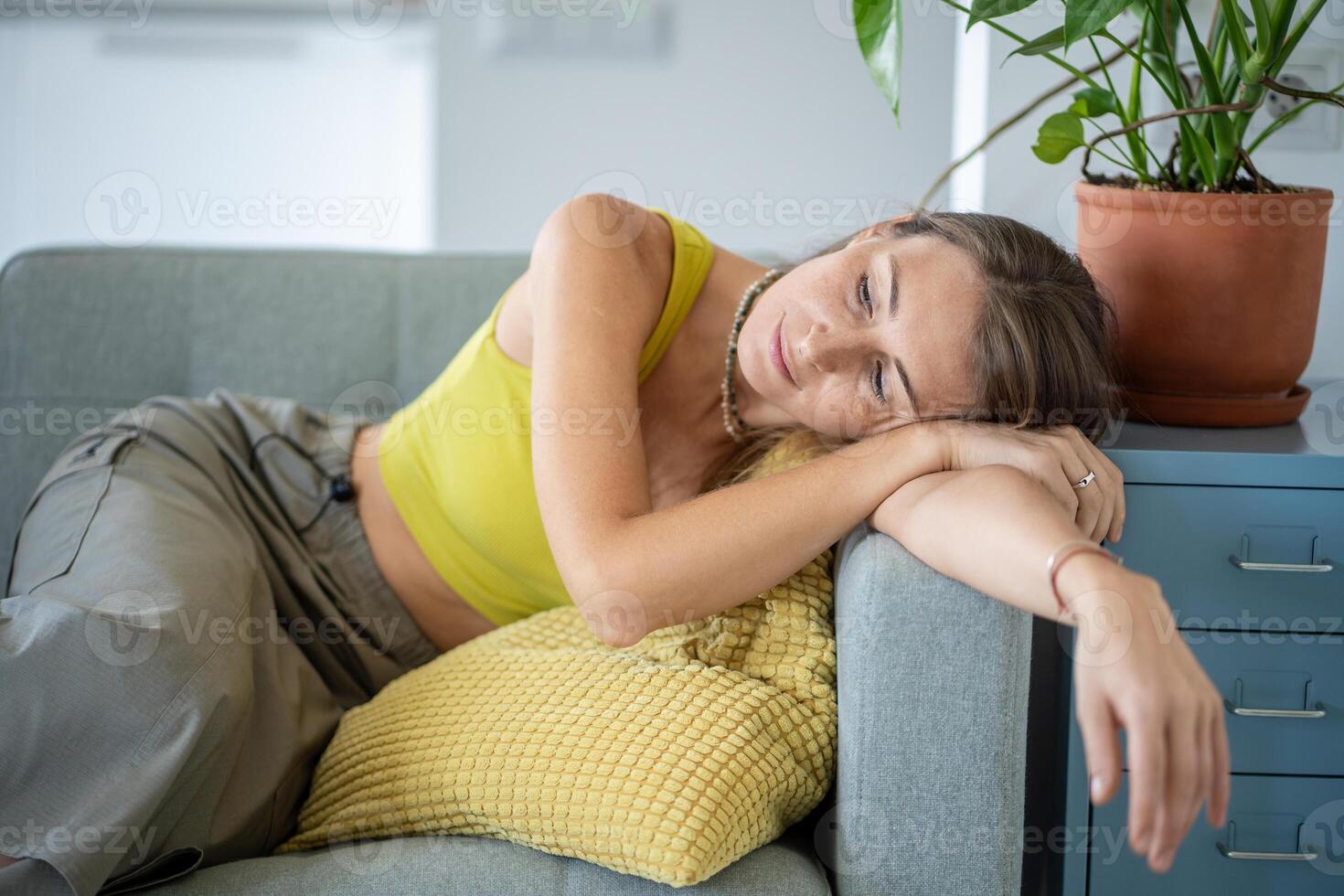 Tired dreaming woman leaning on armrest of sofa resting at home. Thoughtful female relaxing on couch photo