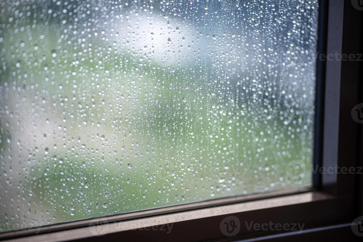 Rain droplets slide down windowpane, sunlight glimmers faintly outside. Overcast weather, depression photo
