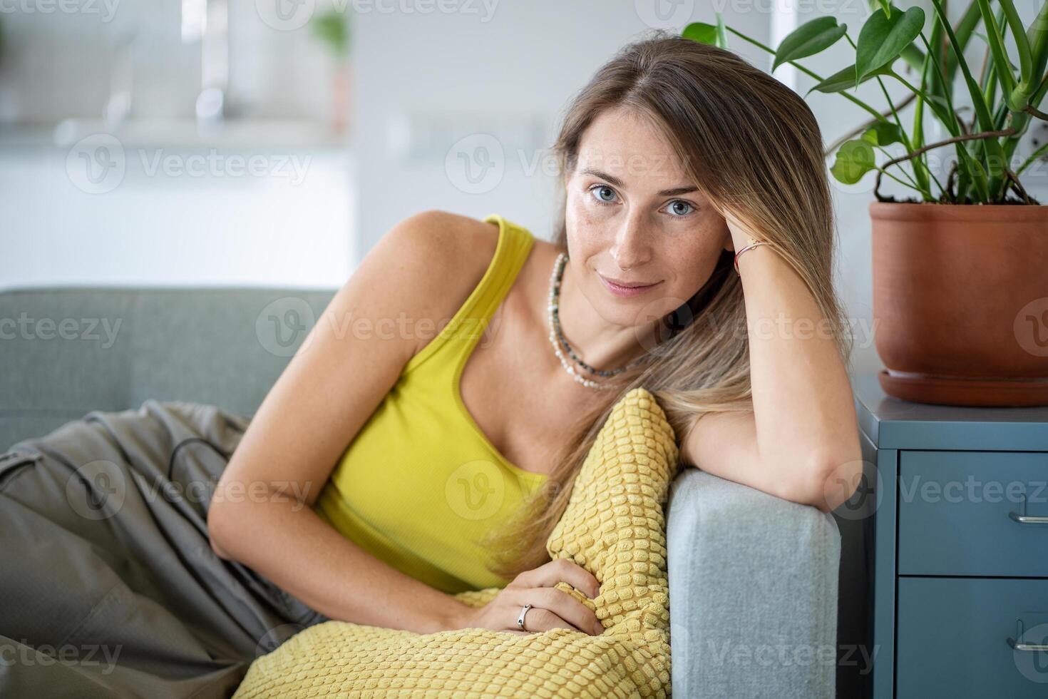 Relaxed woman sitting on sofa spending lazy time at home look at camera with calm emotion. Slow life photo
