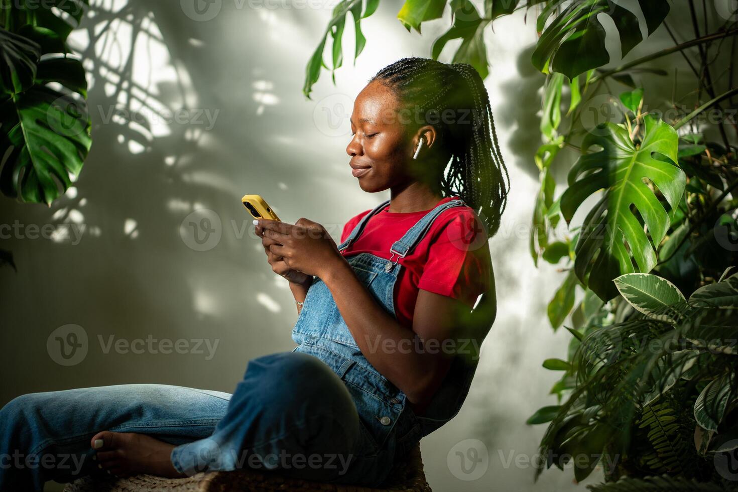 Relaxed black woman in earphones using smartphone at home, selects favourite music track in app. photo