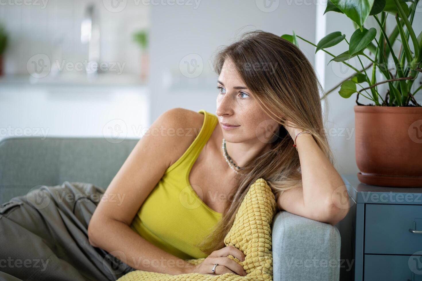 Relaxed woman sitting on sofa spending lazy time at home look at window with calm emotion. Slow life photo