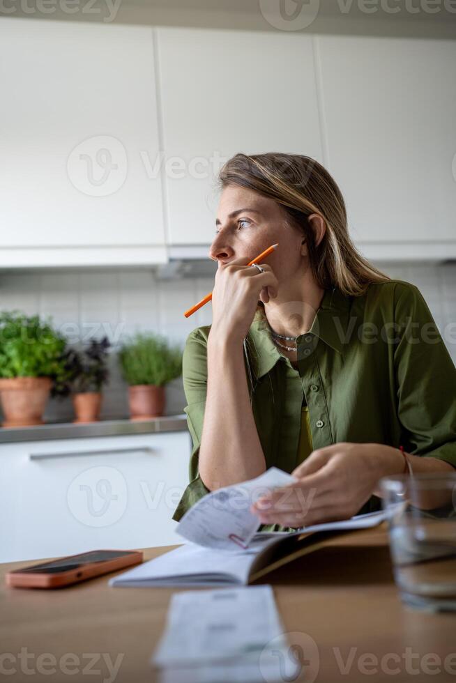 Thoughtful female analysing budget, verifying income and expenses, thinking while looking at window photo