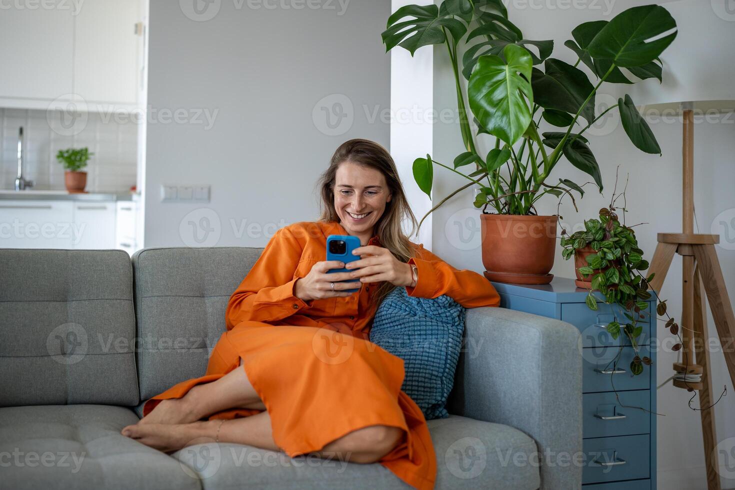 contento mujer utilizando Teléfono móvil a hogar sofá. satisfecho relajado hembra tener Internet divertido, chateando en línea. foto