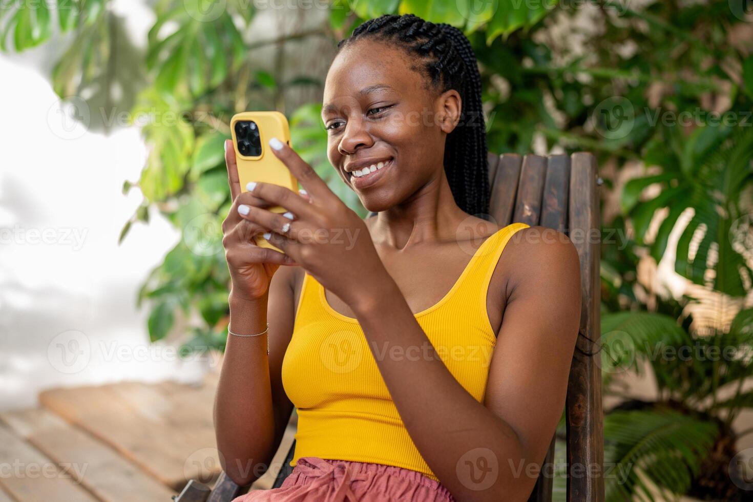 riendo africano americano mujer utilizando teléfono. contento niña relajante a interior hogar urbano selva. foto