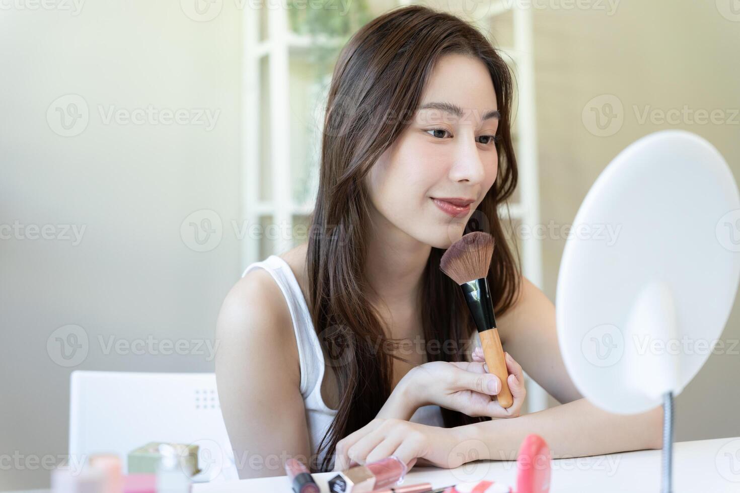 Beautiful Asian woman sit in front of a mirror and smile on makeup. face of a healthy woman applying makeup. Advertisement, lifestyle , cosmetics, makeup accessories, beauty activity, beautician photo