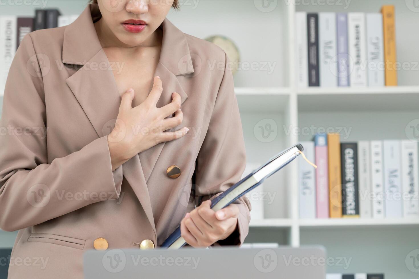 hand hold chest with heart attack symptoms, asian woman working hard have chest pain caused by heart disease, leak, dilatation, enlarged coronary heart, press on the chest with painful expression photo