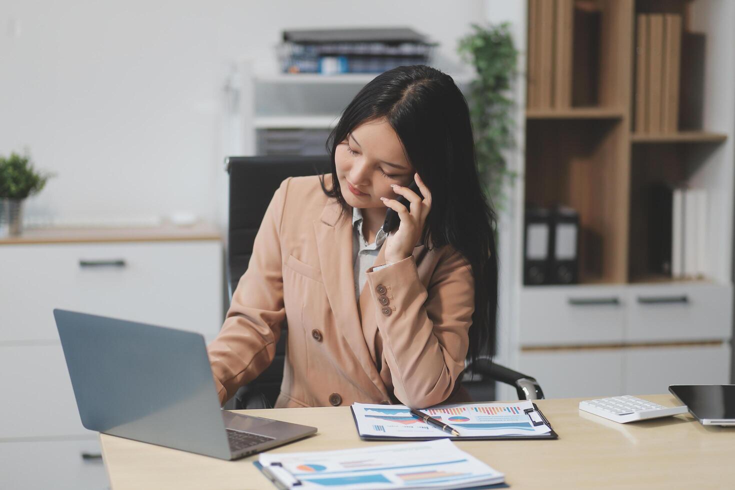 Asian businesswoman in formal suit in office happy and cheerful during using smartphone and working photo