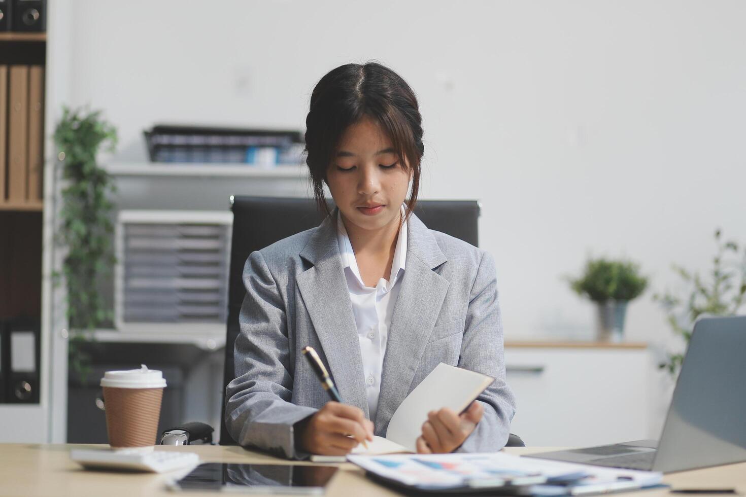 Successful Asian businesswoman smiling using laptop computer and holding coffee cup at office. Confident Asia businesswoman sitting happily in the office. photo