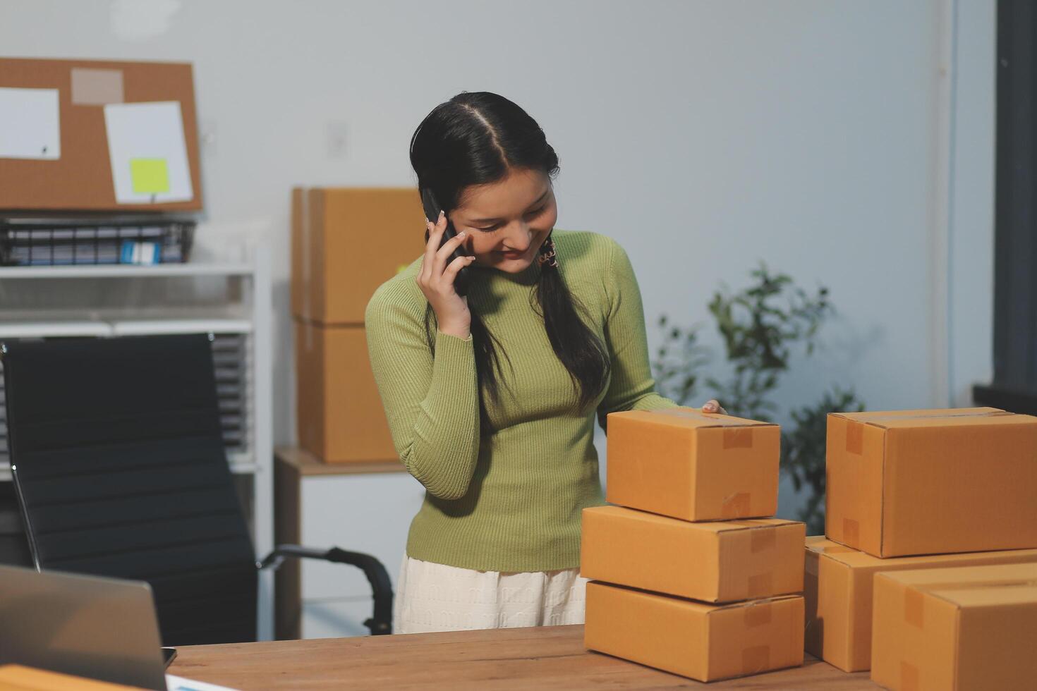 Startup SME small business entrepreneur of freelance Asian woman wearing apron using laptop and box to receive and review orders online to prepare to pack sell to customers, online sme business ideas. photo