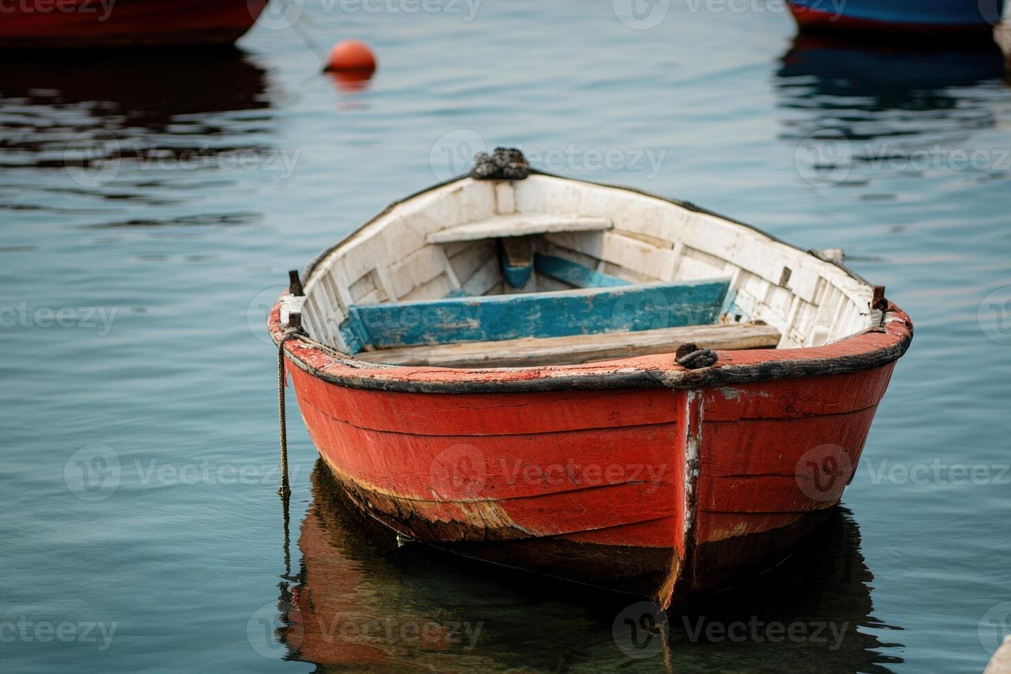 A weathered red rowboat floats in calm waters. photo