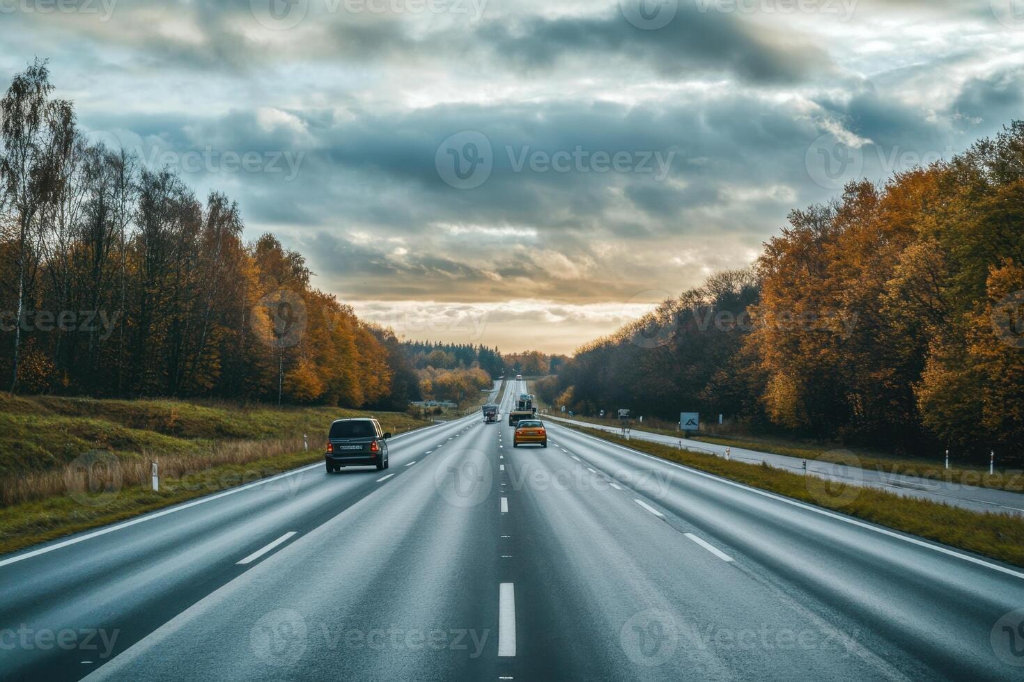 Cars travel on an empty highway with fall foliage on either side. photo