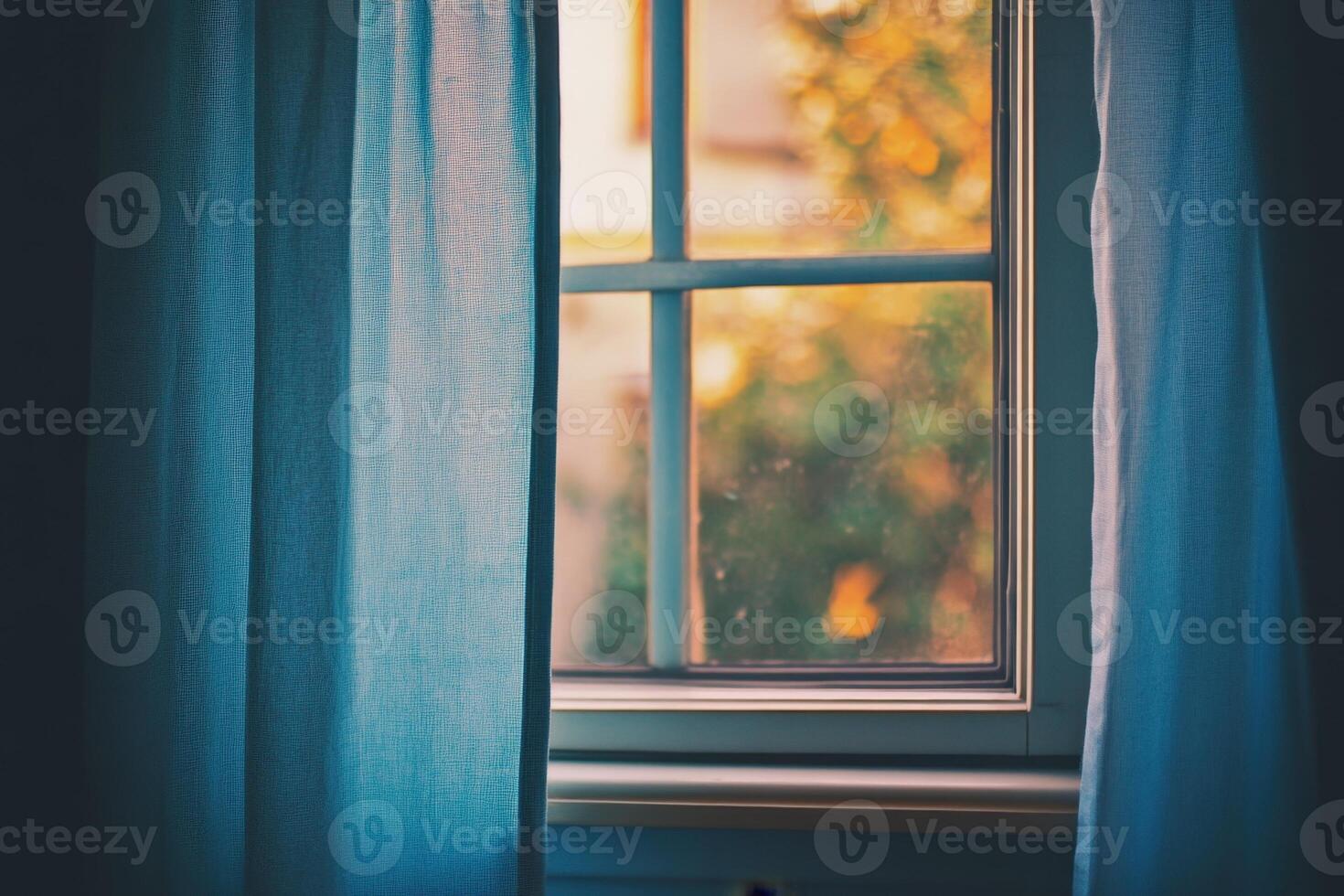 A close up of a window with blue curtains partially drawn, showing a view of a blurry green tree. photo