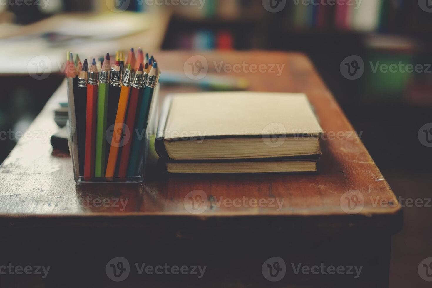A wooden desk with a stack of books, a container of colored pencils, and a blank piece of paper. photo