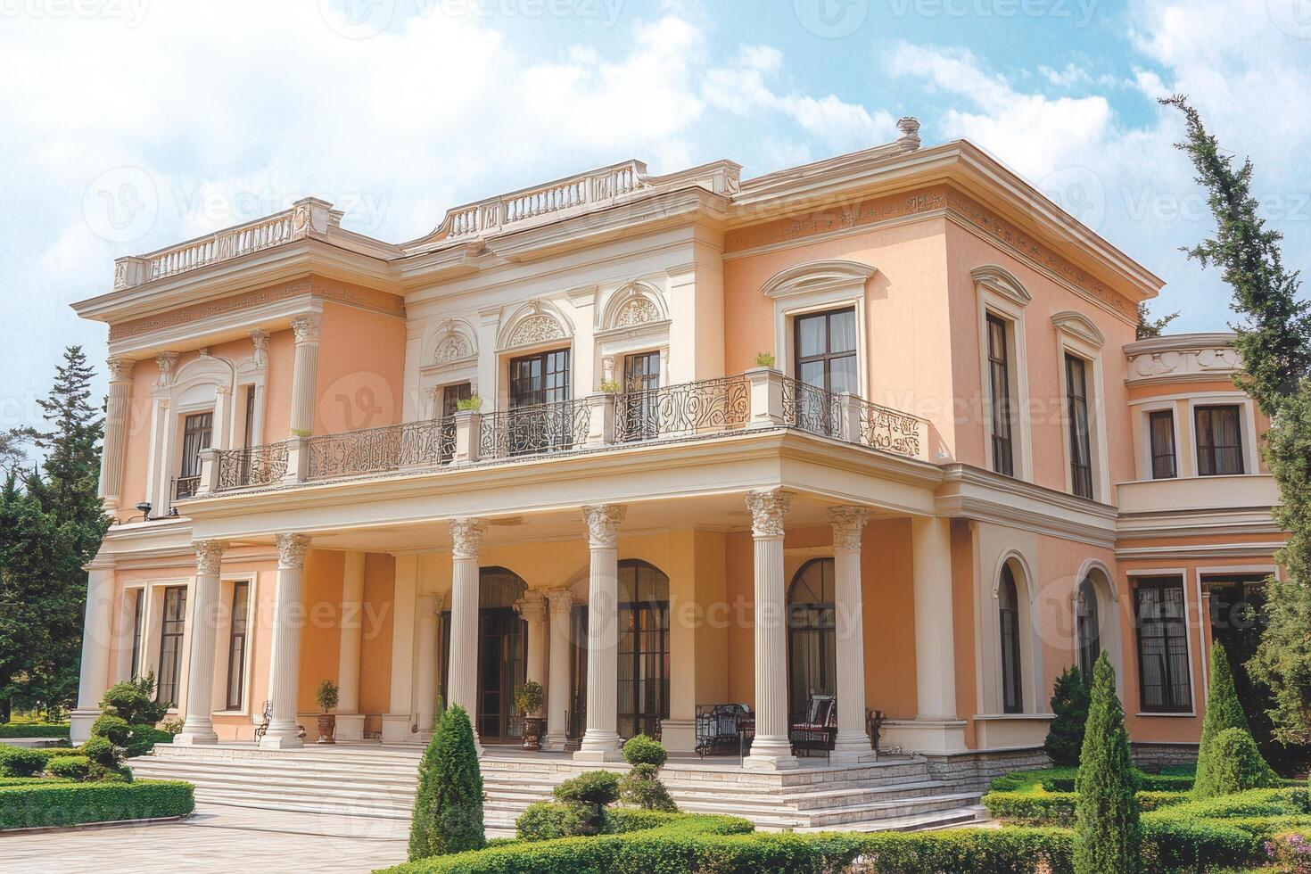 A large, peach-colored mansion with white trim and columns, surrounded by manicured lawns and shrubs. photo