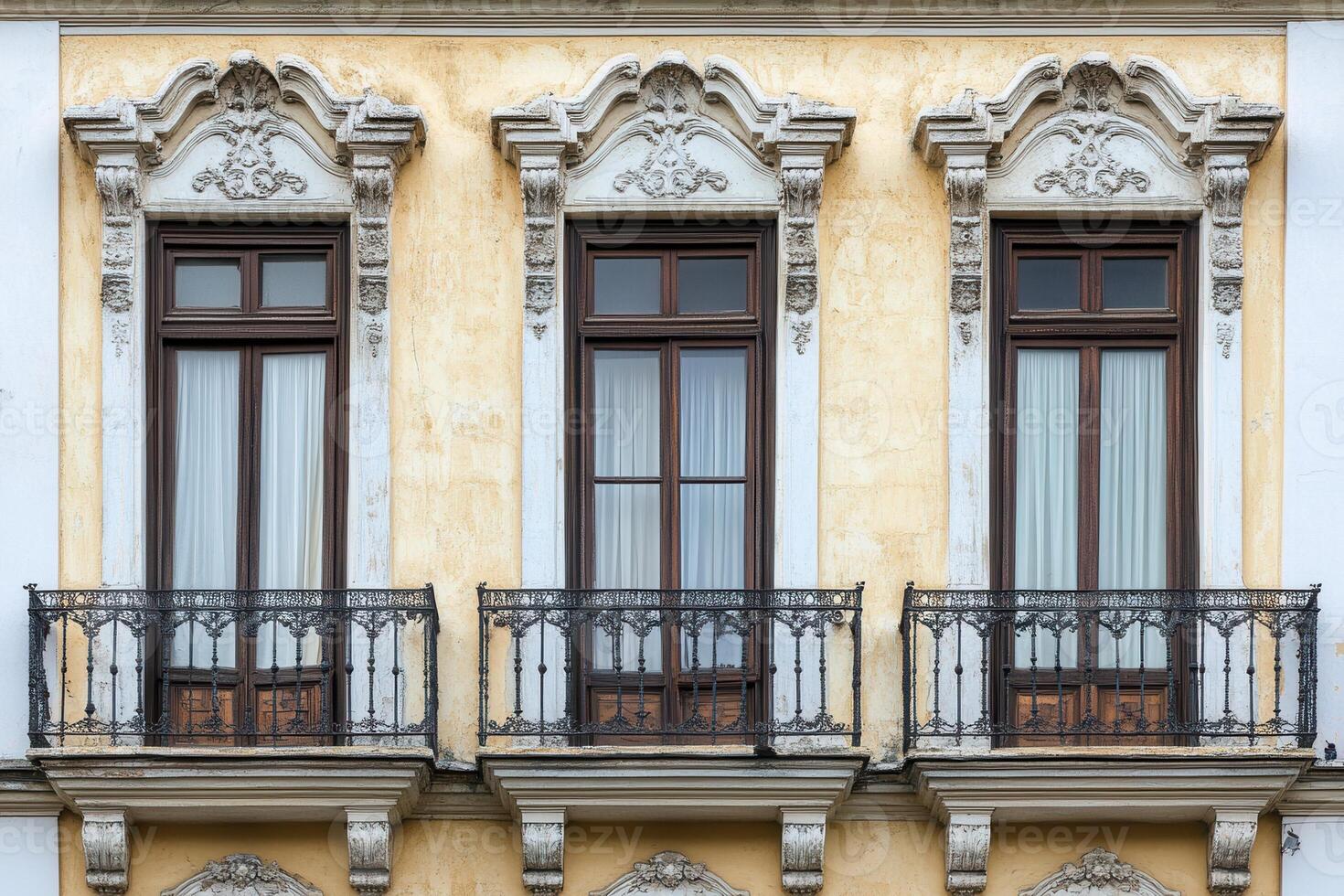 Three windows with balconies on a yellow building. photo