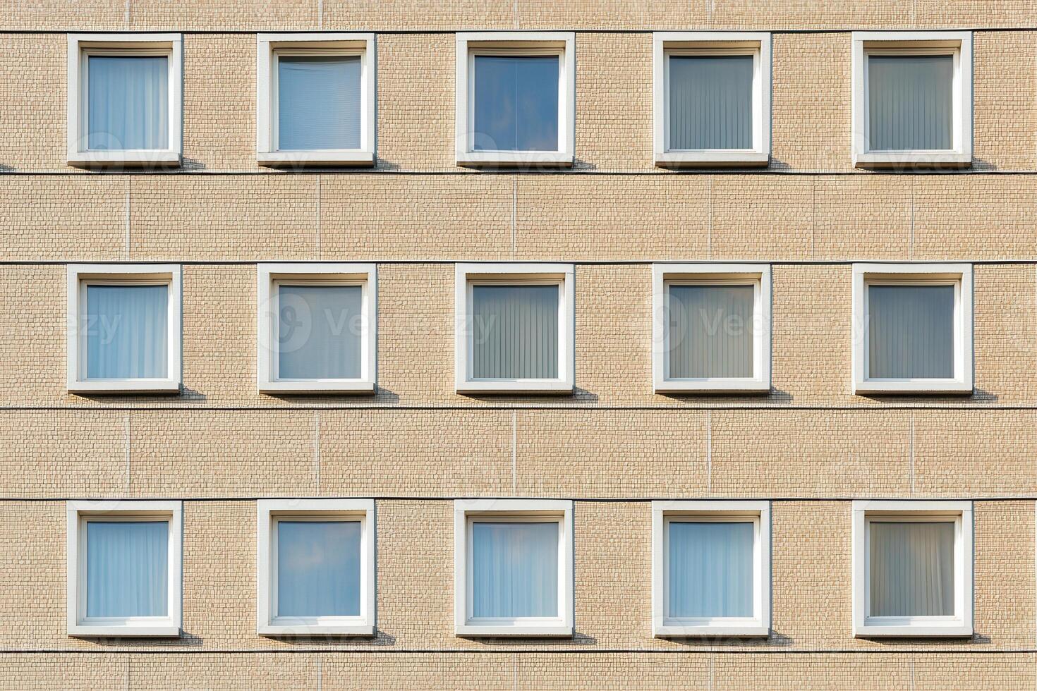Beige building facade with white framed windows in a symmetrical pattern. photo
