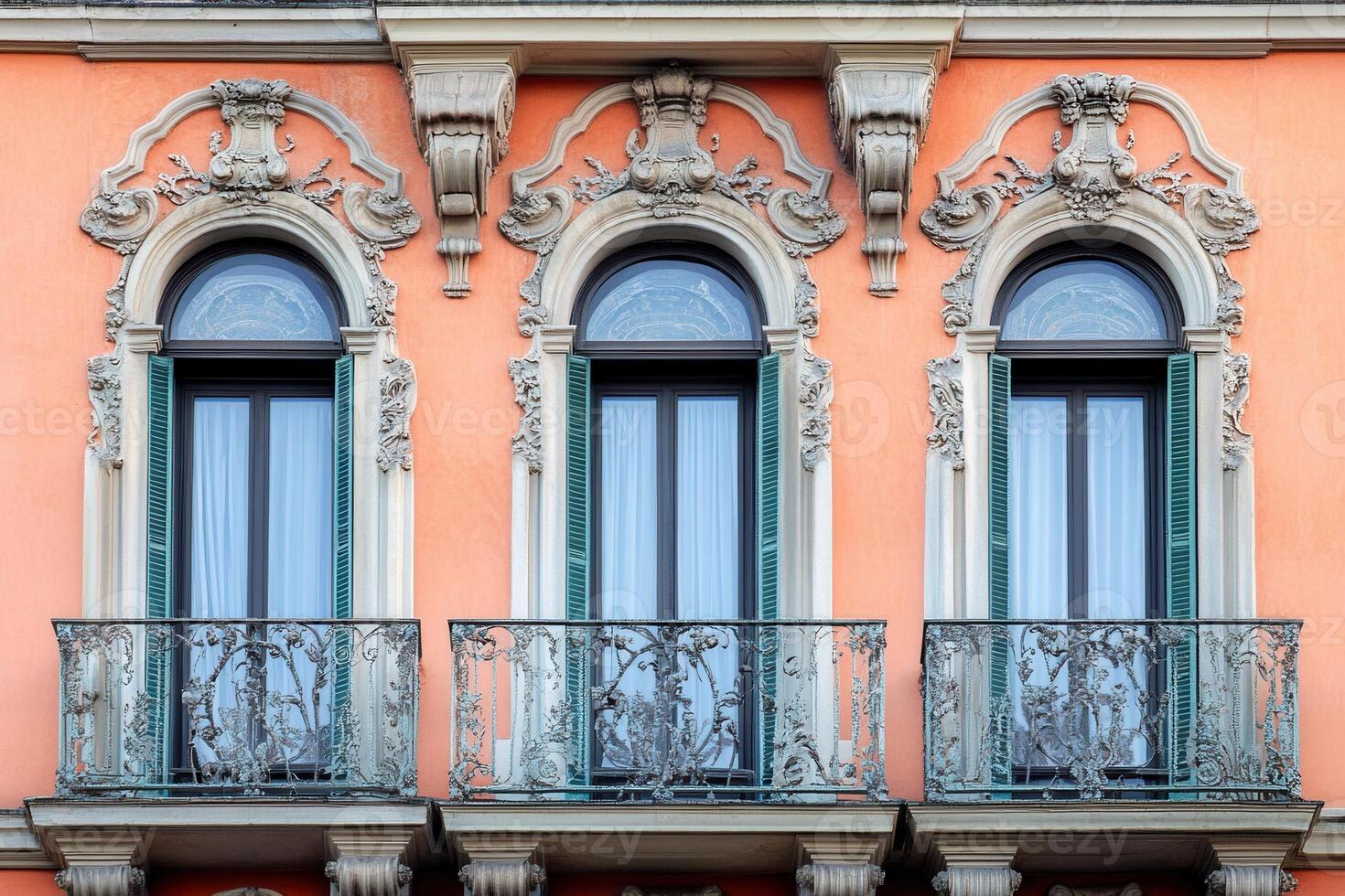 Three ornate windows with balconies on a peach building facade. photo