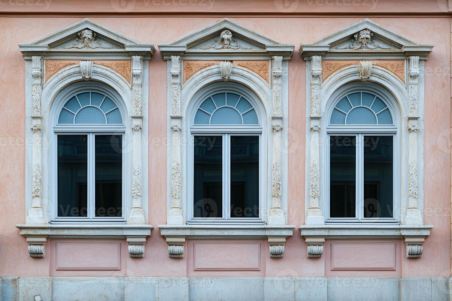 Three arched windows with ornate frames on a pink building facade. photo