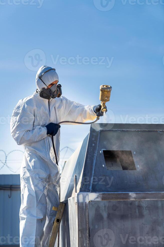 Man painting in suit. Worker in white suit finishing with paint. photo