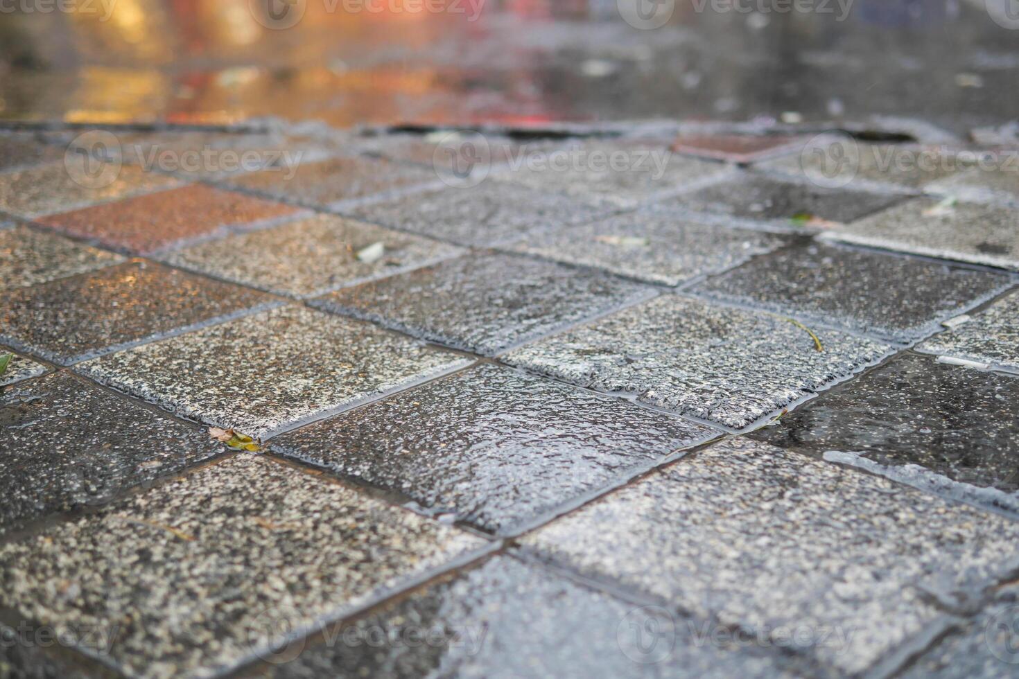 A wet, paved surface exhibiting highly reflective tiles during rainy weather conditions photo
