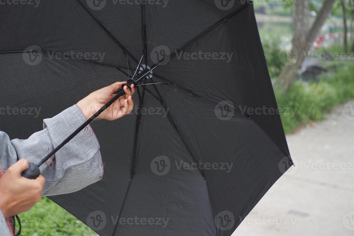 A CloseUp Shot of Hands Skillfully Opening a Classic Black Umbrella Against the Rainy Atmosphere photo
