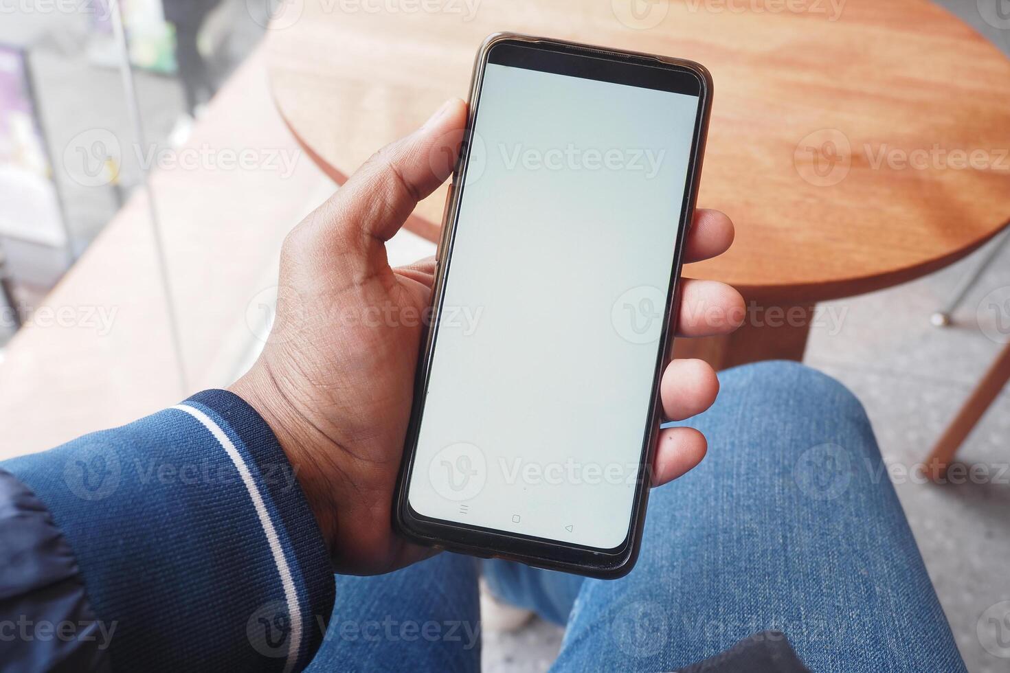 A person sits in a cozy cafe, holding a smartphone with a blank screen, hinting at engagement photo