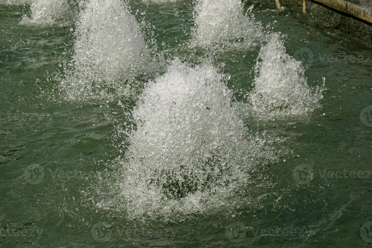 Close-up view of streams of fountain with reflection and lens flare. Water jet. City fountain. Water pressure. How to survive the heat. Splashes shining in the sun. Selective shallow focus. photo