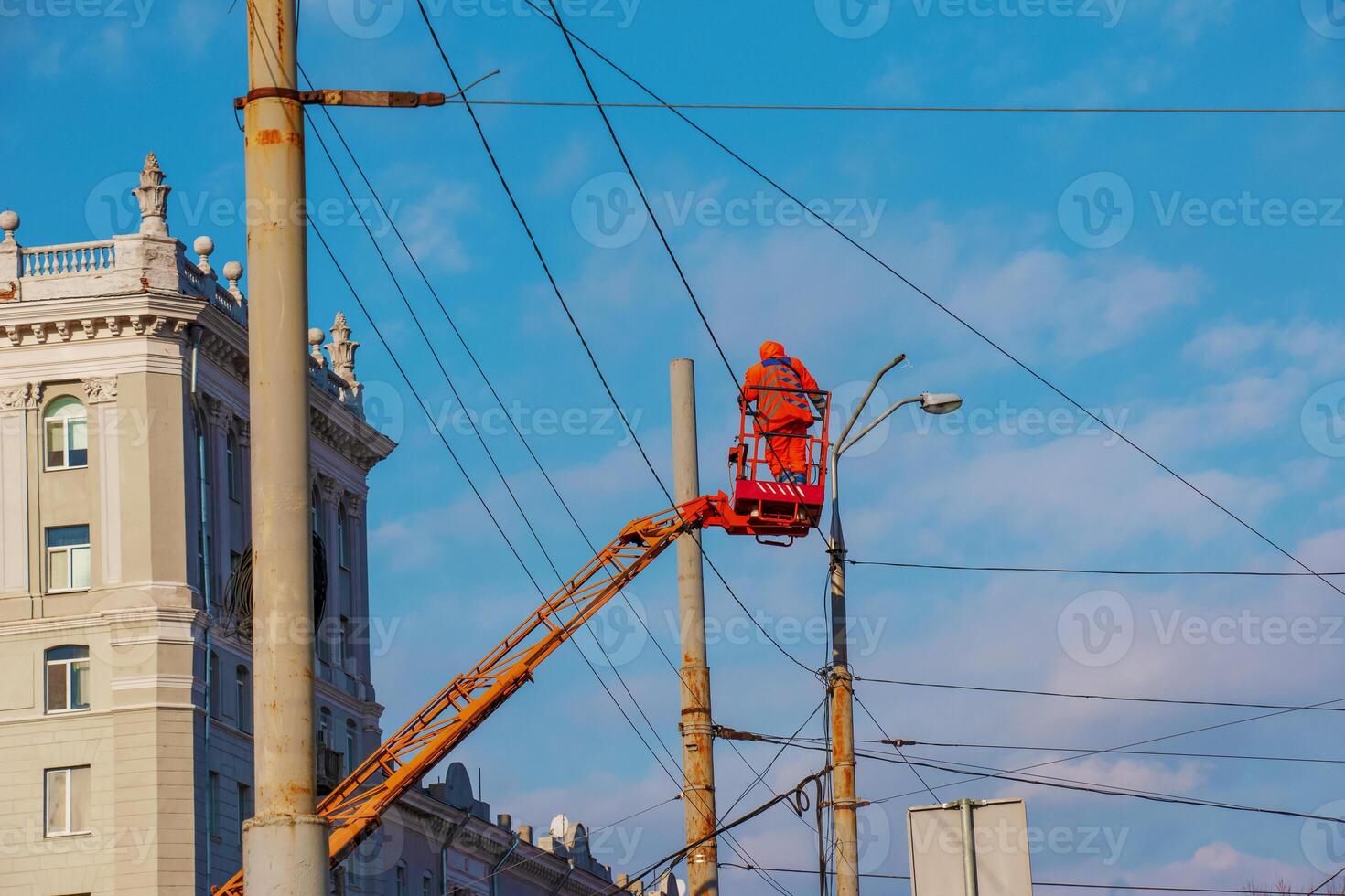 Electrician repairing wire of the power line with bucket hydraulic lifting platform on blue sky photo