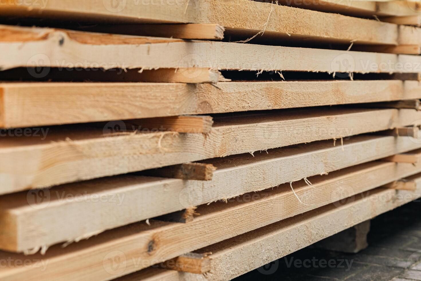 Stack of wooden boards. The boards appear rough-cut with visible knots and uneven edges. The wood been stacked for drying or storage. photo
