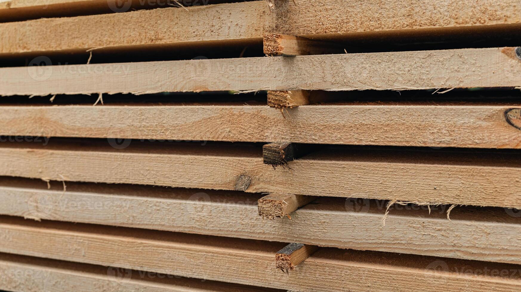 Stack of wooden boards. The boards appear rough-cut with visible knots and uneven edges. The wood been stacked for drying or storage. photo