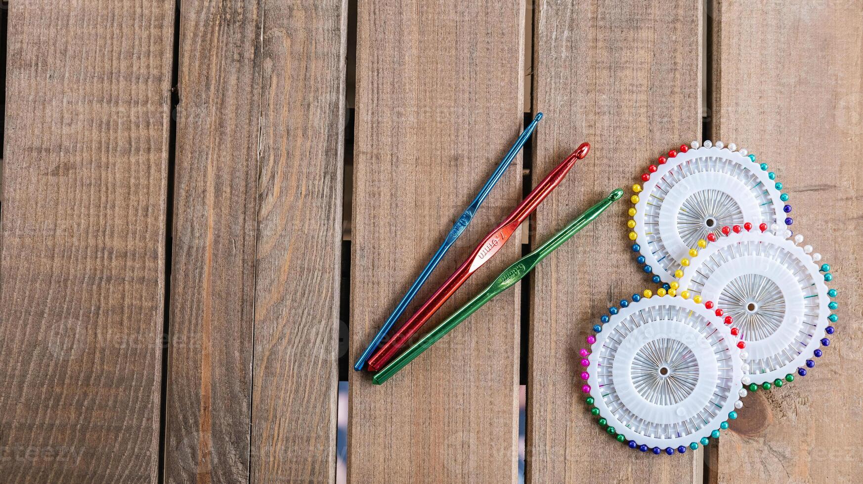 Set of colorful crochet hooks and several wheels of sewing pins arranged neatly on a wooden surface. photo