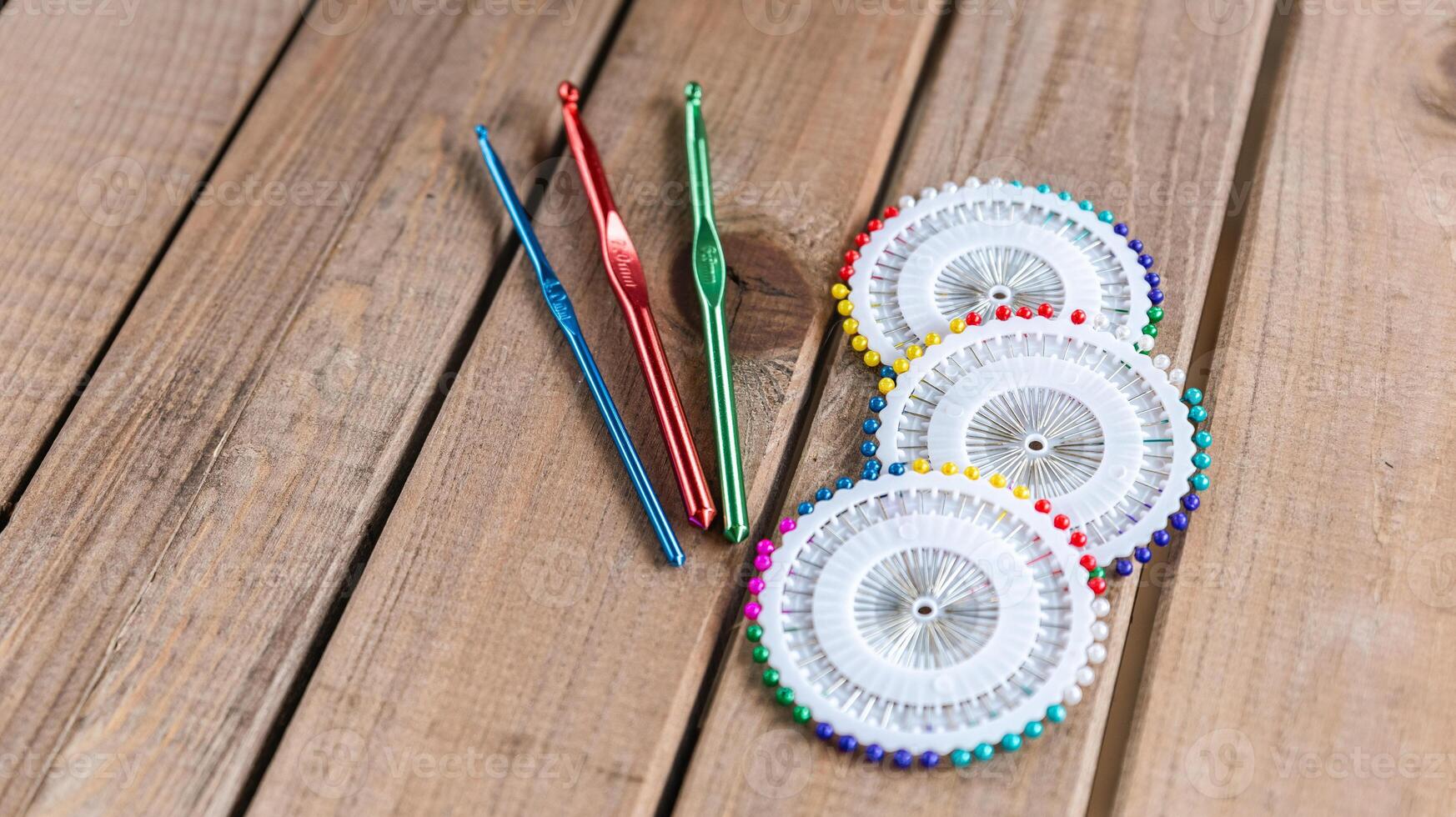Set of colorful crochet hooks and several wheels of sewing pins arranged neatly on a wooden surface. photo