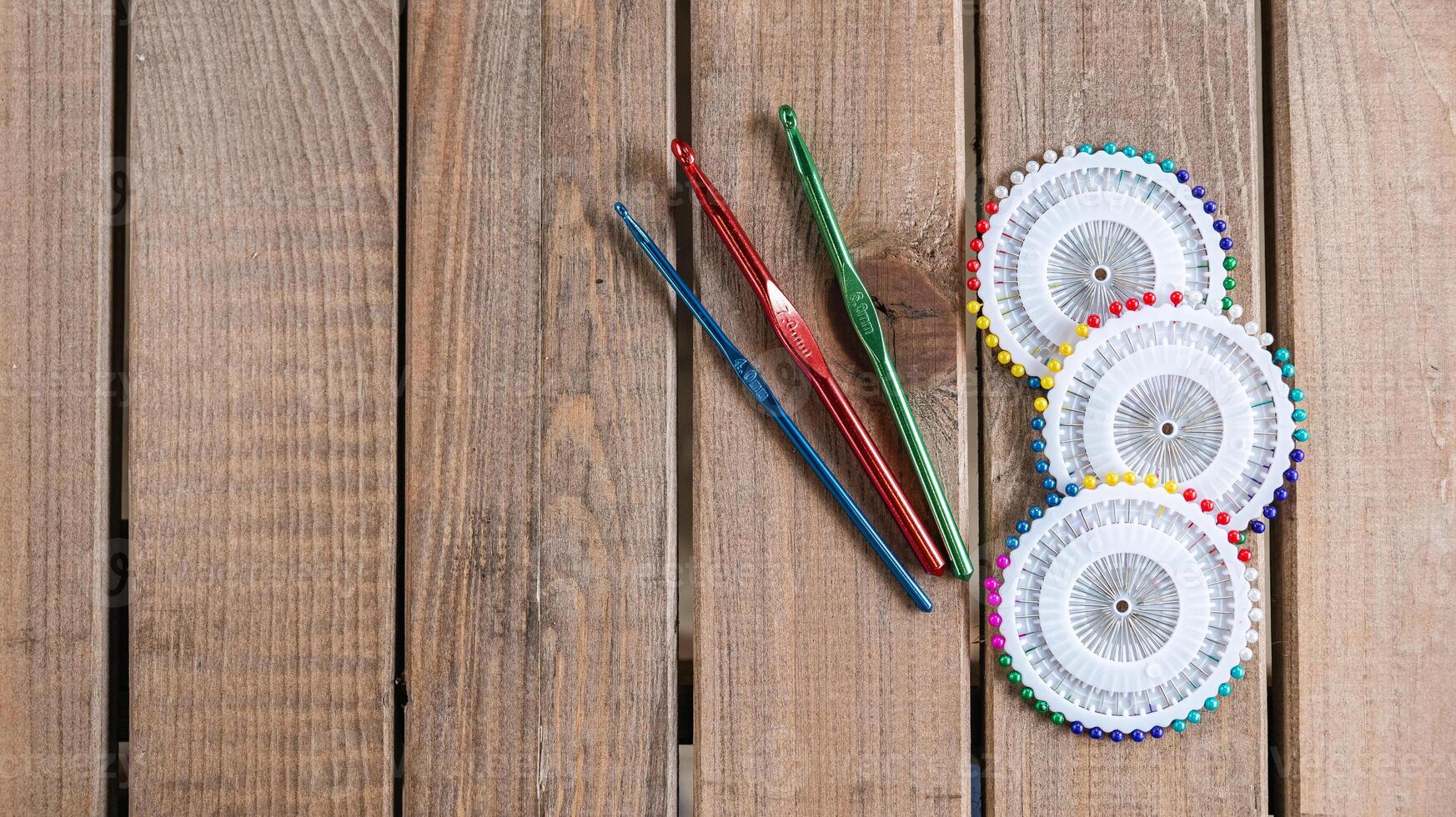 Set of colorful crochet hooks and several wheels of sewing pins arranged neatly on a wooden surface. photo