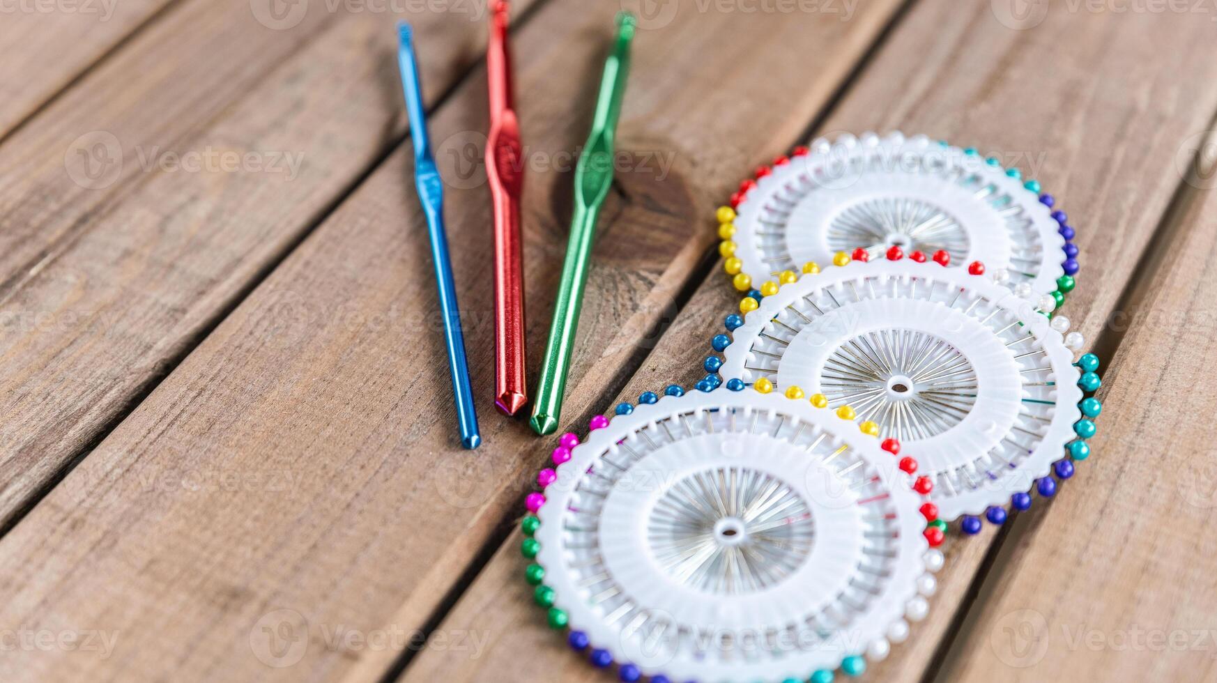 Set of colorful crochet hooks and several wheels of sewing pins arranged neatly on a wooden surface. photo