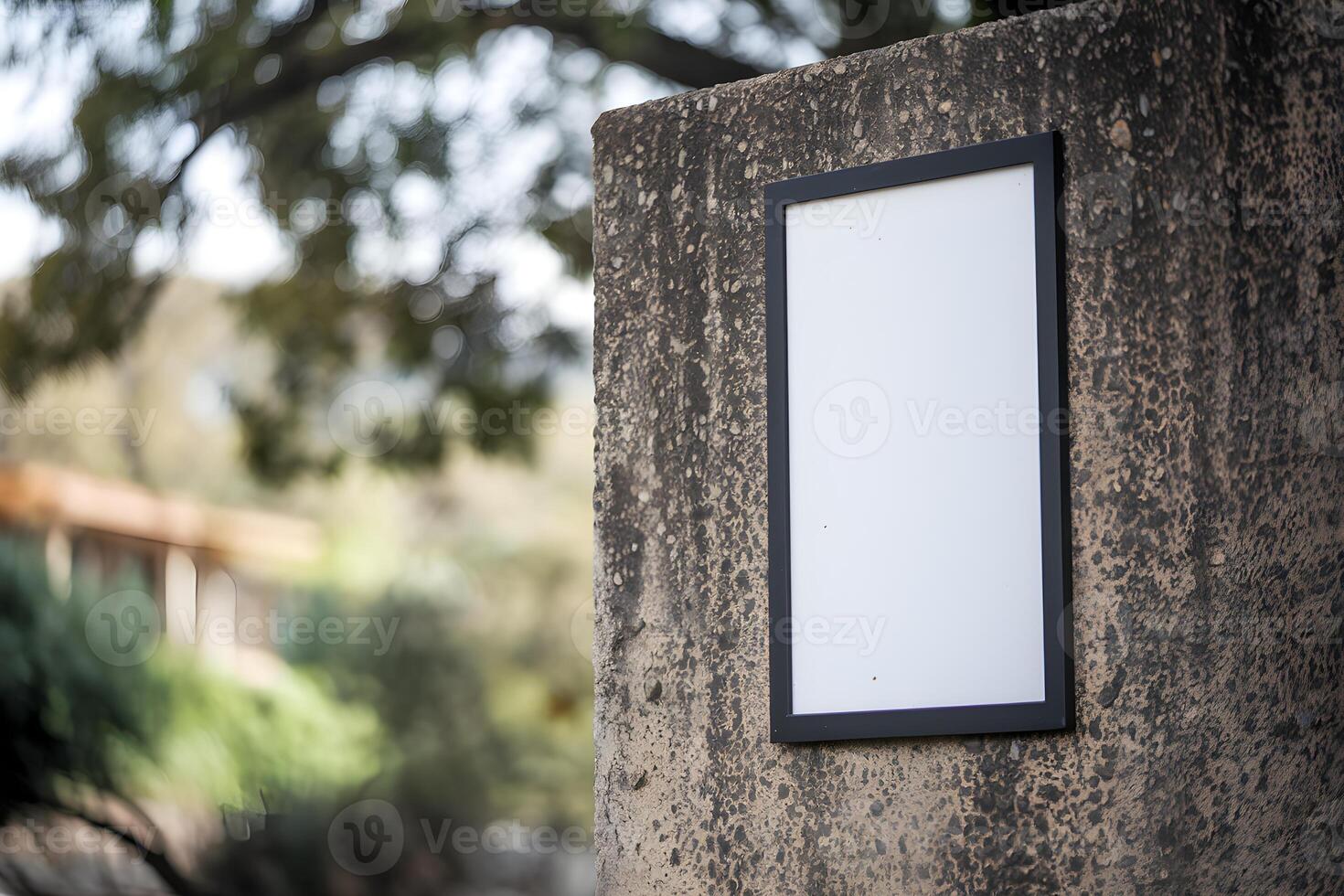 White signboard with black frame mounted on concrete wall, trees slightly blurred behind photo