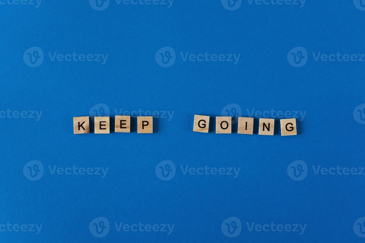 The phrase keep going is lined with wooden letters on a blue background top view. Postcard in place for text. Flatlay. The words. photo
