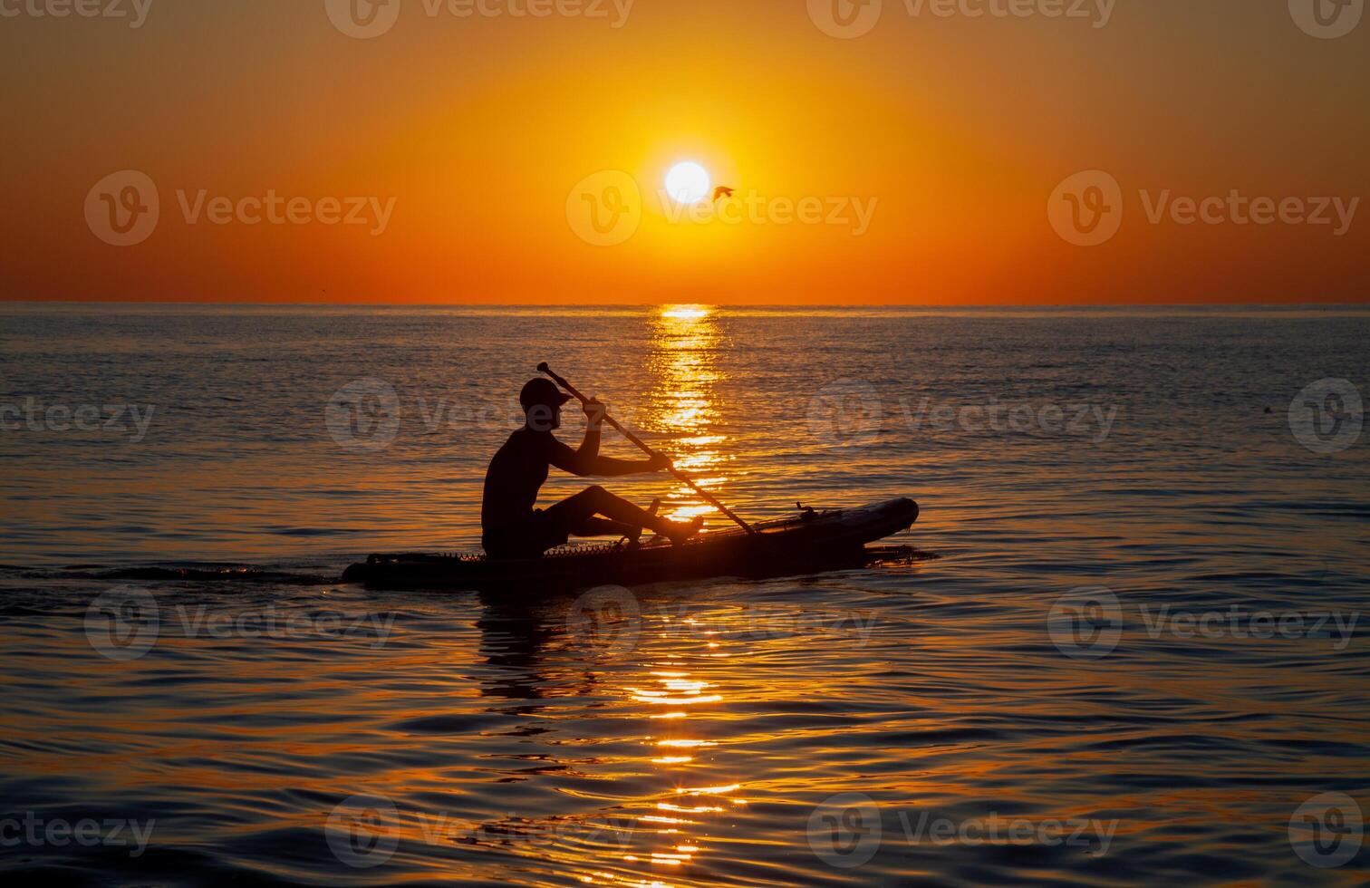 Silhouette of a man floating on a board with an oar. Dawn sun on the sea. Swimming on a supboard. Water active sports. Beautiful landscape. Sunset on the sea. Ocean coast. Copy space. photo