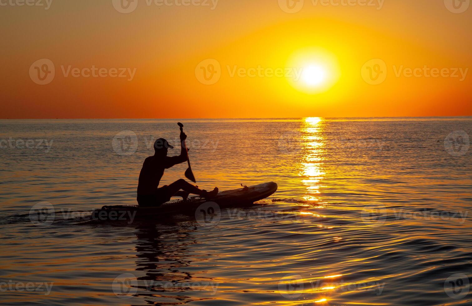 Silhouette of a man floating on a board with an oar. Dawn sun on the sea. Swimming on a supboard. Water active sports. Beautiful landscape. Sunset on the sea. Ocean coast. Copy space. photo