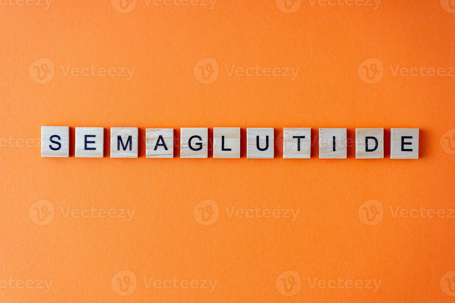Word semaglutide. The phrase is laid out in wooden letters top view. Orange flat lay background. photo