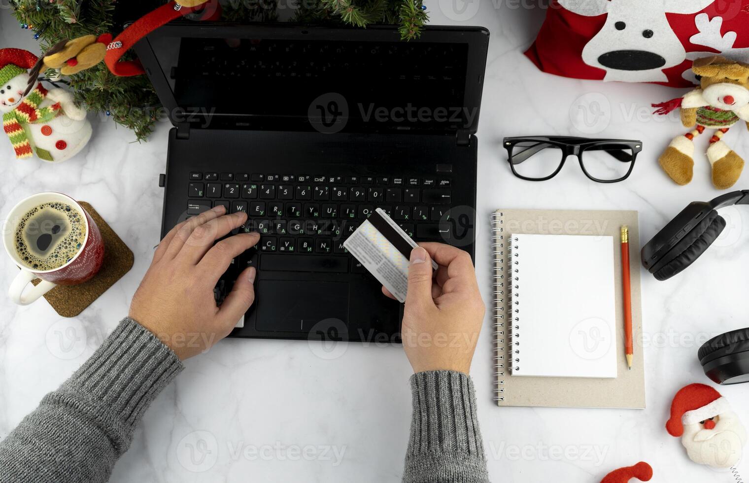Christmas online shopping. Purchase of goods and gifts for the new year via the Internet. Write a list and hold a credit card. Work desk with laptop and holiday decorations. Man's hands. Copy space. photo
