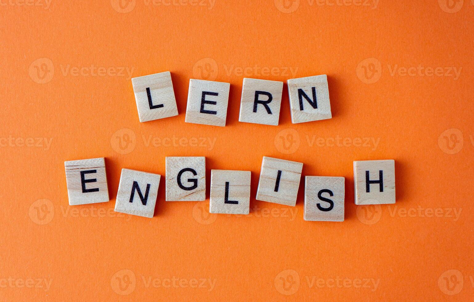 Word learn English. Motivation. The phrase is laid out in wooden letters top view. Motivation. Orange flat lay background. photo