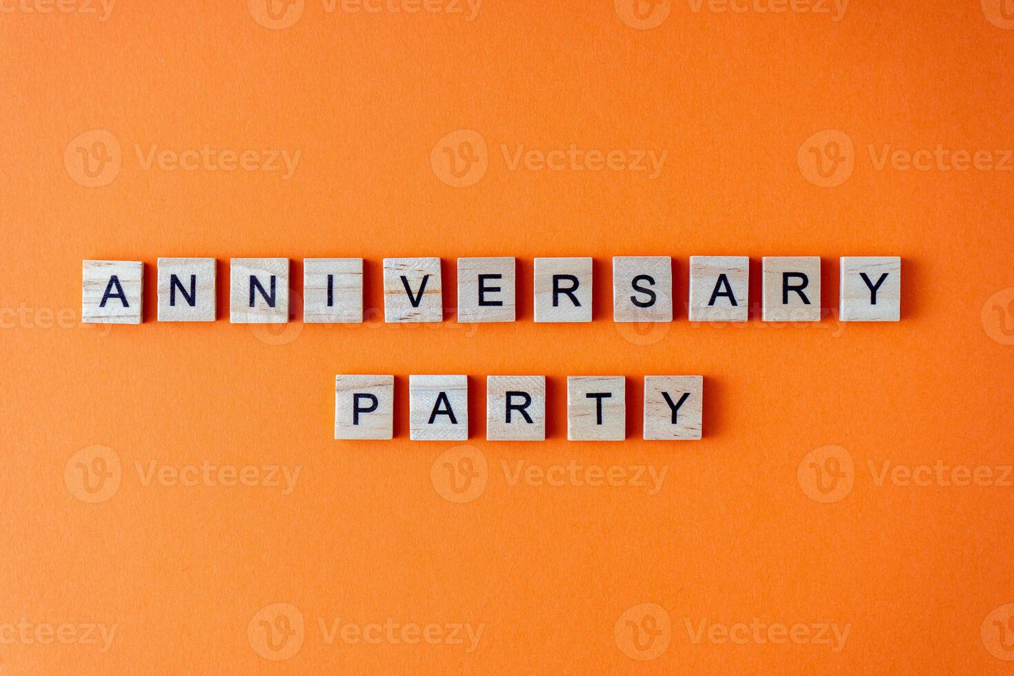 Anniversary party word. The phrase is laid out in wooden letters top view. Orange flat lay background. photo